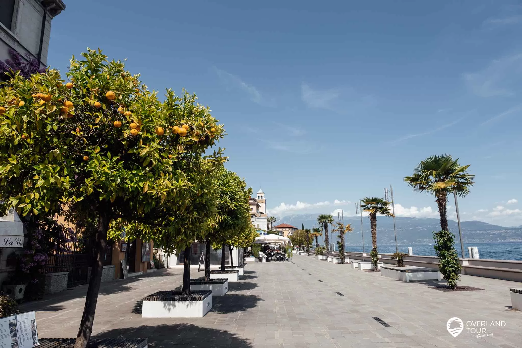 Blick auf die Uferpromenade von Gardone Riviera am Gardasee mit Palmen und historischen Hotelbauten