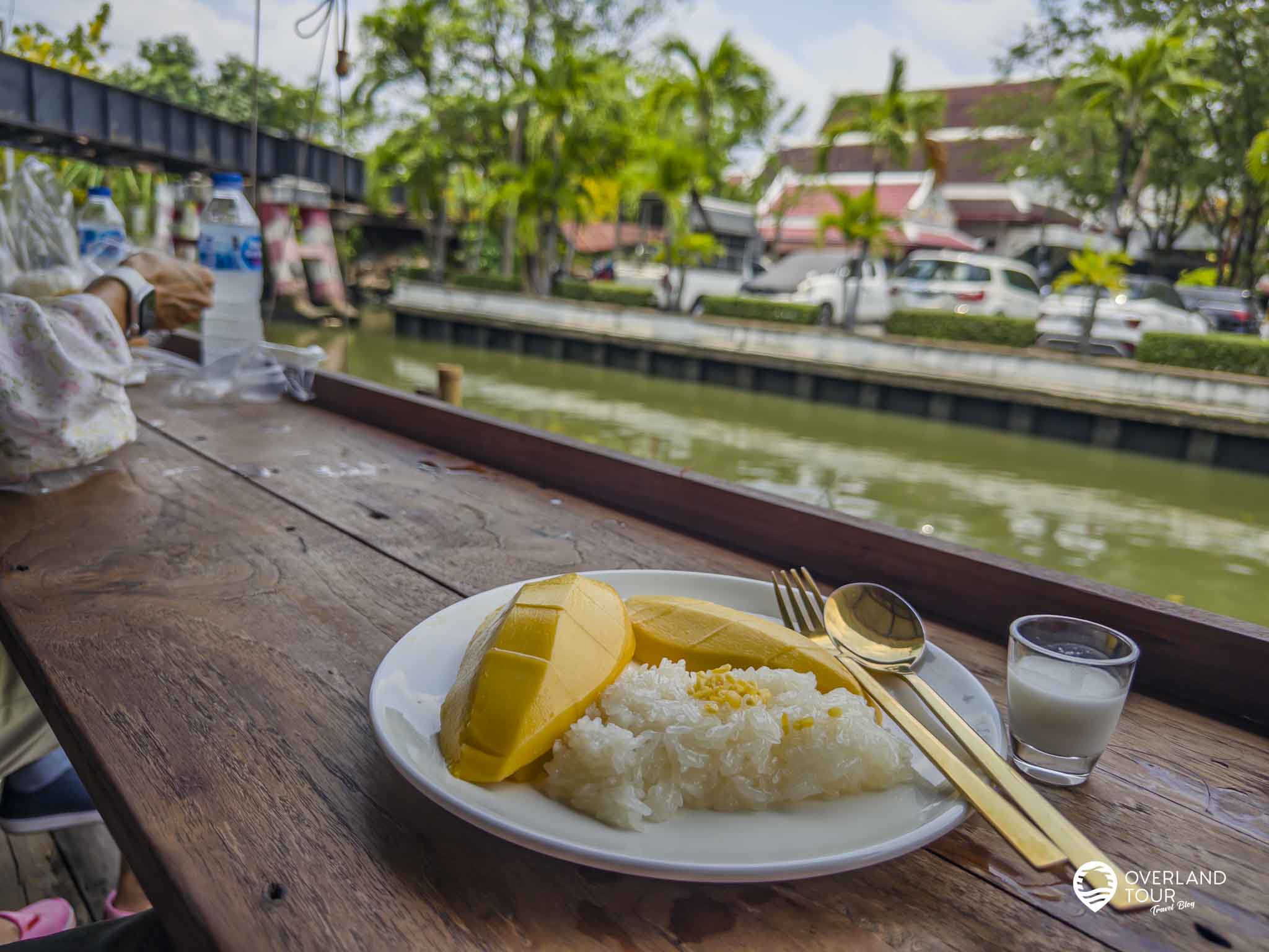 Khao Niew Moon Pa Nee: Bangkoks bester Mango Sticky Rice Ein Teller mit einer goldenen Mango und dem Sticky Rice samt einem kleinen Behälter mit Kokosmilch sind auftrappiert am Khlong