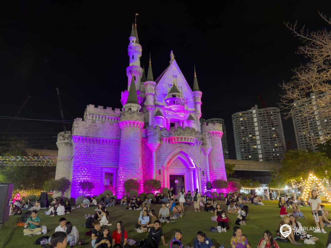 Märchenstunde in Bangkok: Wenn das Schloss in bunten Farben erstrahlt, verwandelt sich die Rasenfläche in ein gemütliches Lichtermeer. Hier zelebrieren die Locals ihre Picknick-Kultur - entspannt, authentisch und fernab vom Großstadtstress